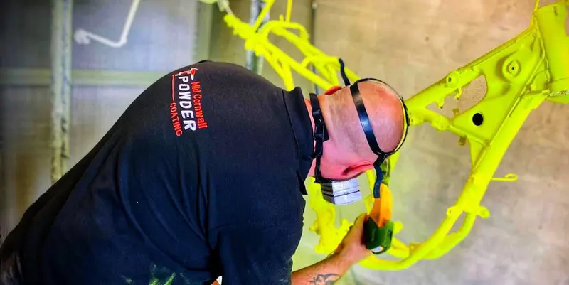 Powder coater applying coating to a motorcycle frame Mid Cornwall Powder Coating Bodmin