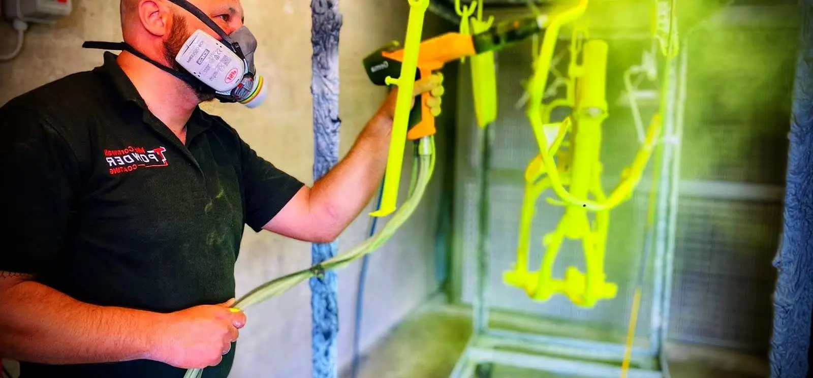 Powder coater spraying a motorcycle frame in the booth at Mid Cornwall Powder Coating Bodmin